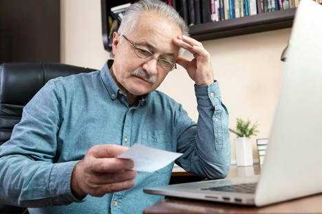 Anxious looking elderly man looking at a paper with a computer next to him